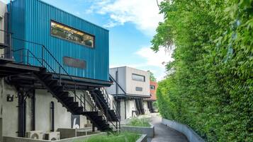 Un edificio moderno con fachada azul, una escalera y un camino al lado de un seto verde.