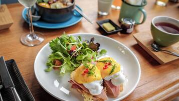 Ein Frühstücksteller mit Eggs Benedict, einer grünen Tasse Tee und einer Salatschüssel auf einem Holztisch.