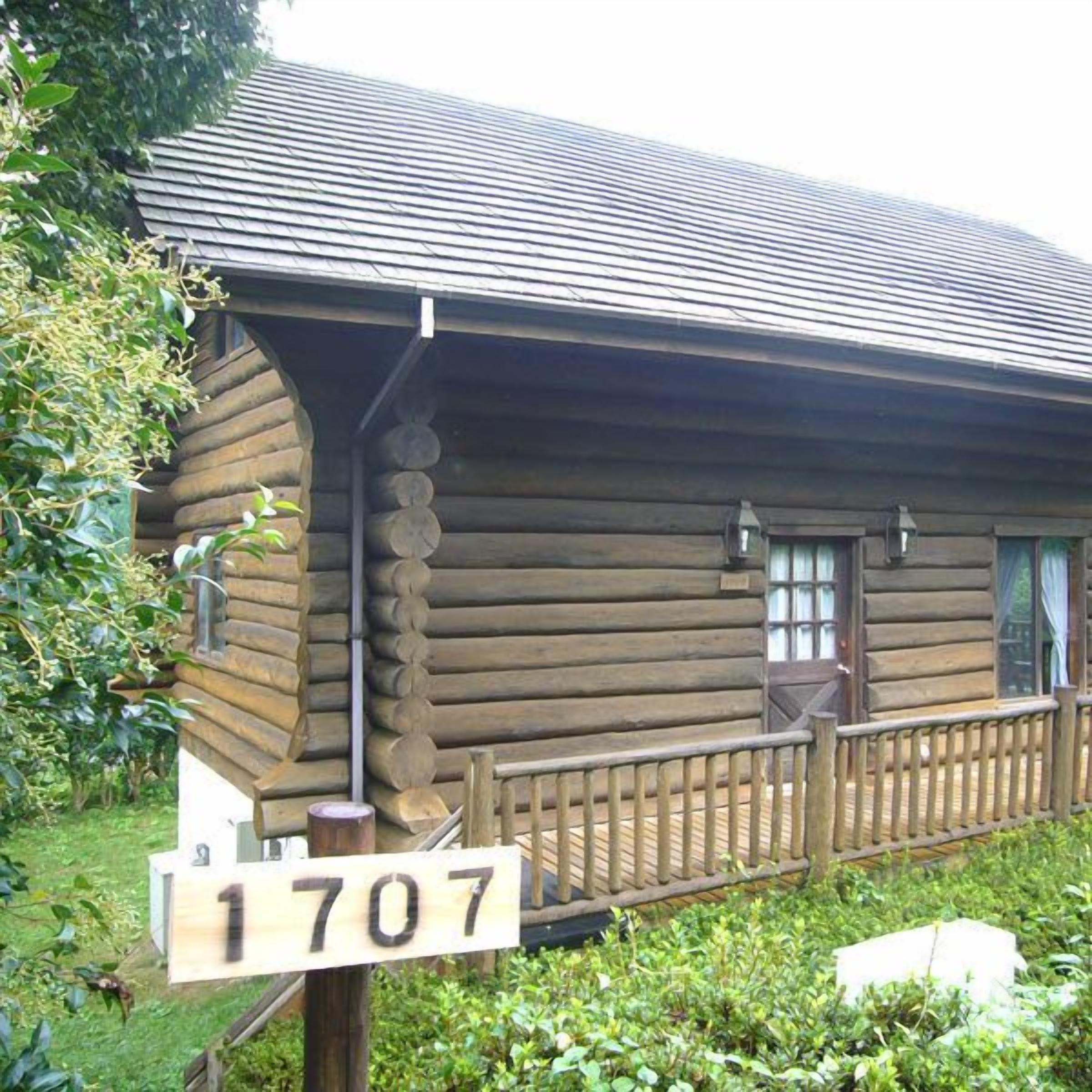 A log cabin with a wooden porch and a number sign '1707' in front.