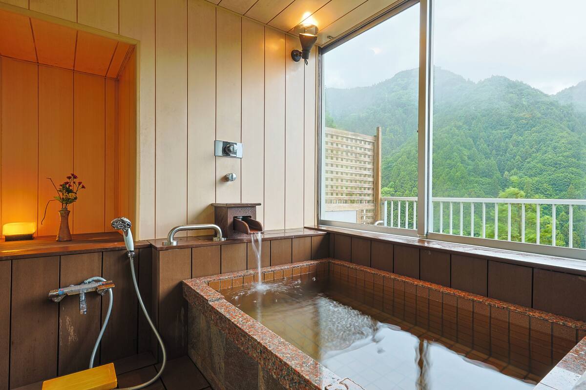 A wooden cabin with a large window overlooking a forested mountain.