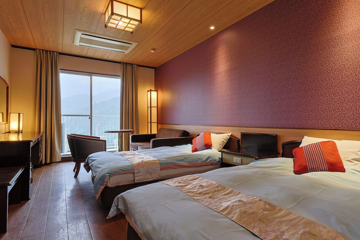 A hotel room with two beds, a desk, a chair, and a TV.