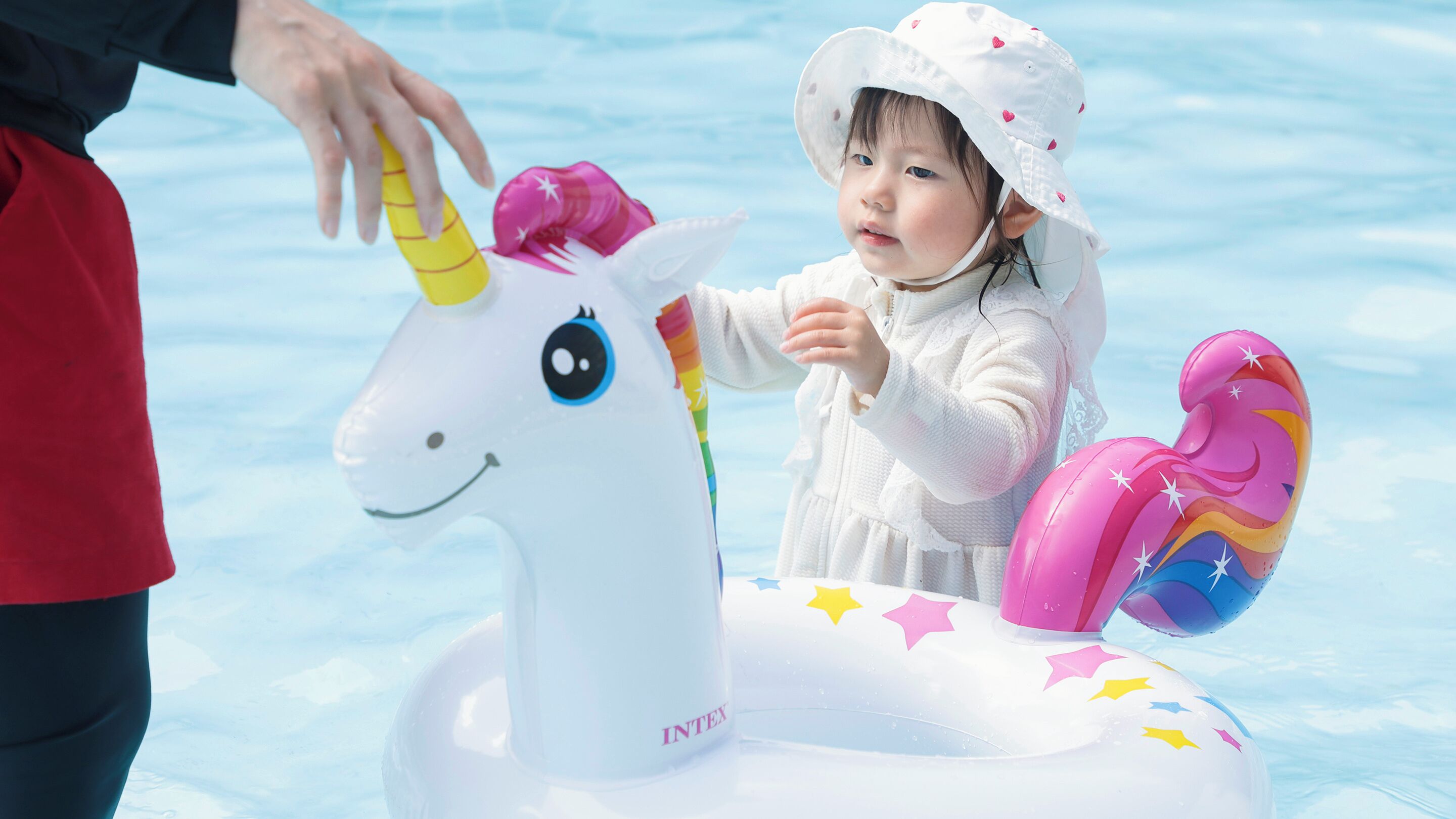A child in a white outfit with a unicorn float in a pool.
