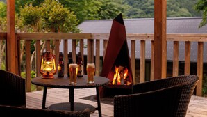 A wooden deck with a round table, wicker chairs, a lantern, and a fire pit. - Hinotanionsen Misugi Resort (Tsu)