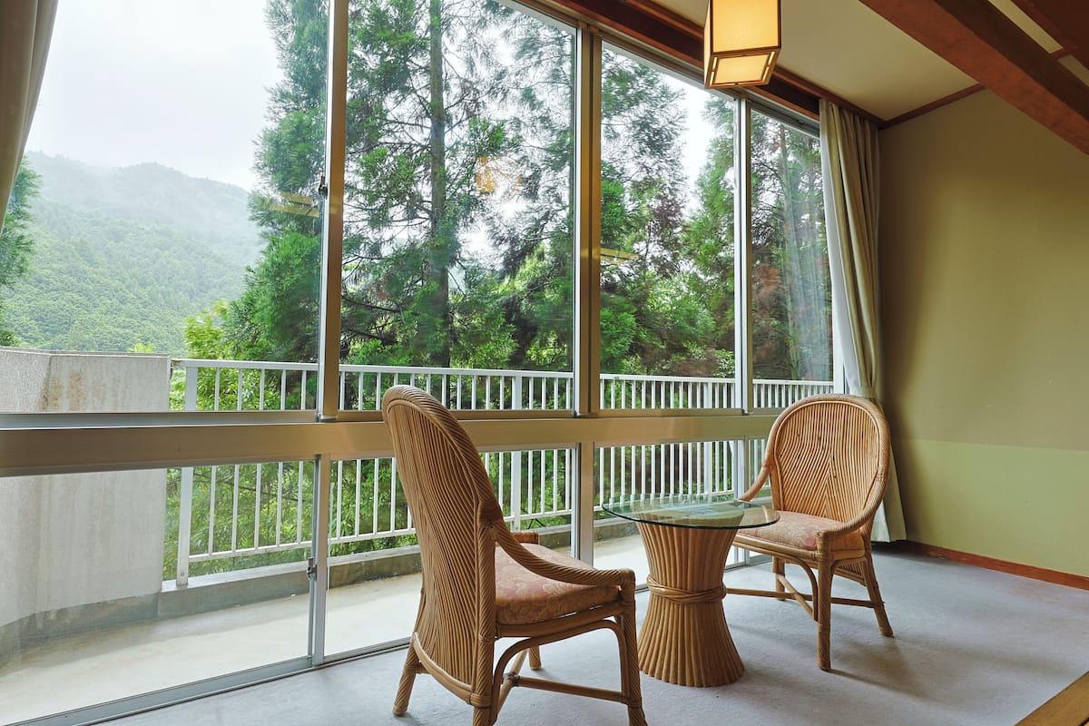 A balcony with wicker chairs and a glass table, overlooking a forested mountain.