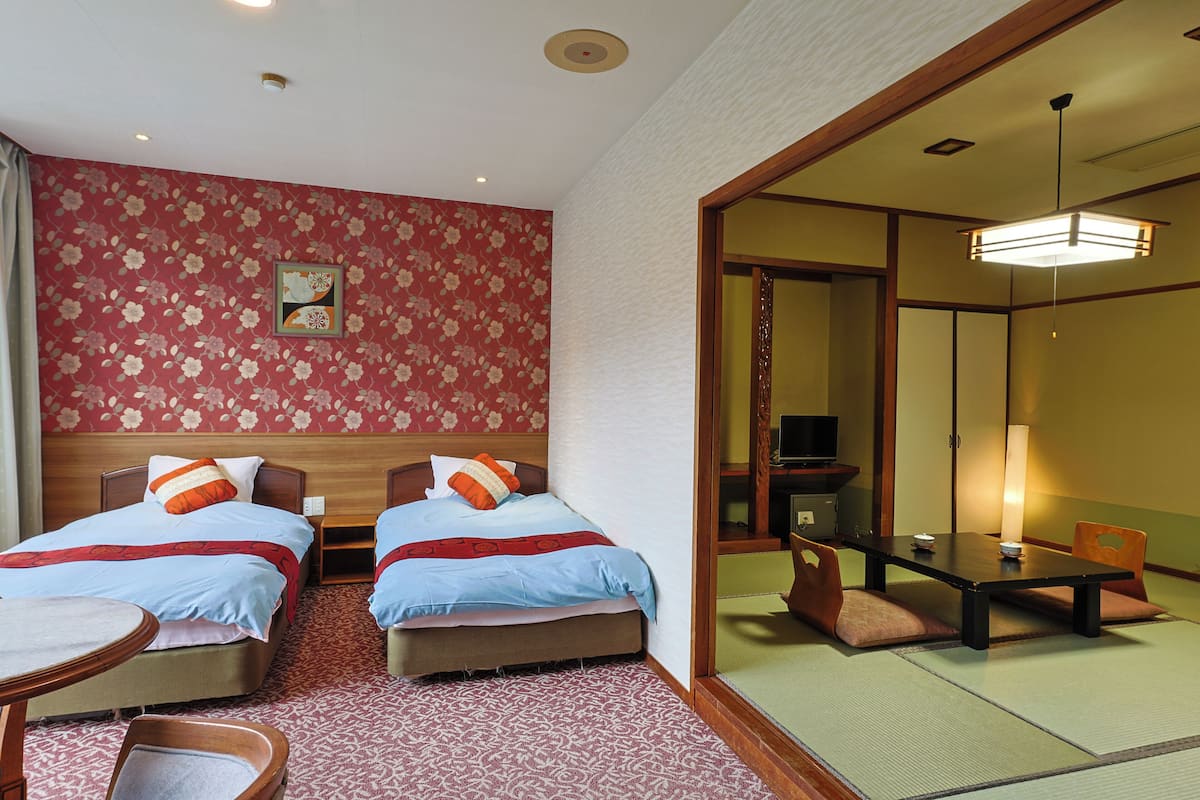 A hotel room with two beds, a dining table, and a traditional Japanese-style room.