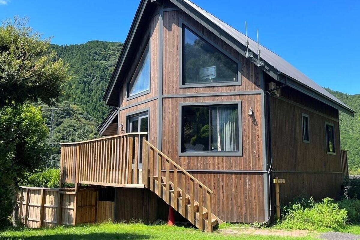 A two-story wooden house with a balcony, large windows, and a steeply pitched roof.