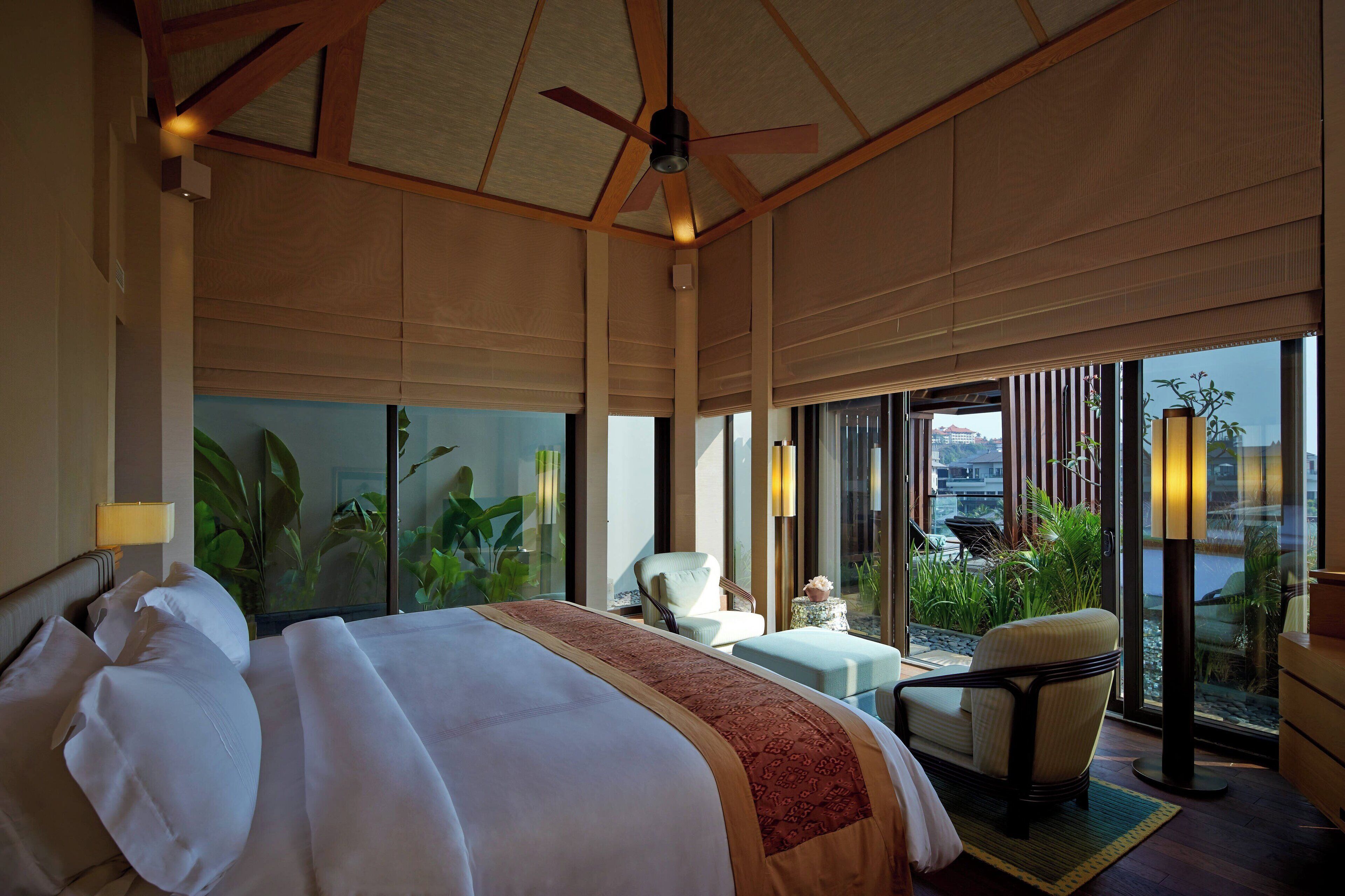 A spacious bedroom with a large bed, a ceiling fan, and a view of a balcony with plants.