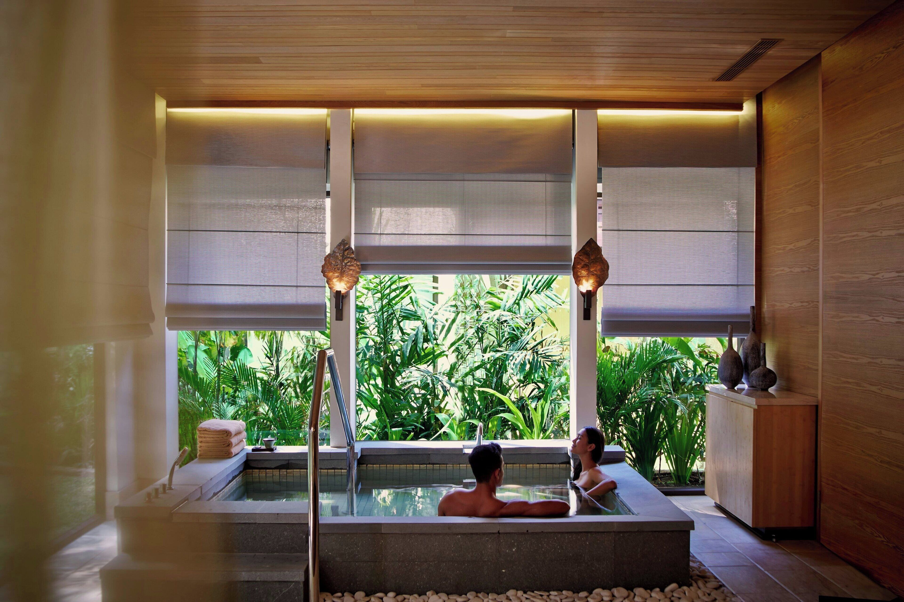 Un espacio de spa con hidromasaje, paneles de madera y ventanas amplias con vistas a la vegetación.