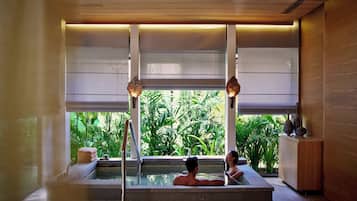 Un espacio de spa con hidromasaje, paneles de madera y ventanas amplias con vistas a la vegetación.