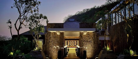 A modern building entrance with a stone facade, a checkered pattern wall, and a pathway leading to the entrance.