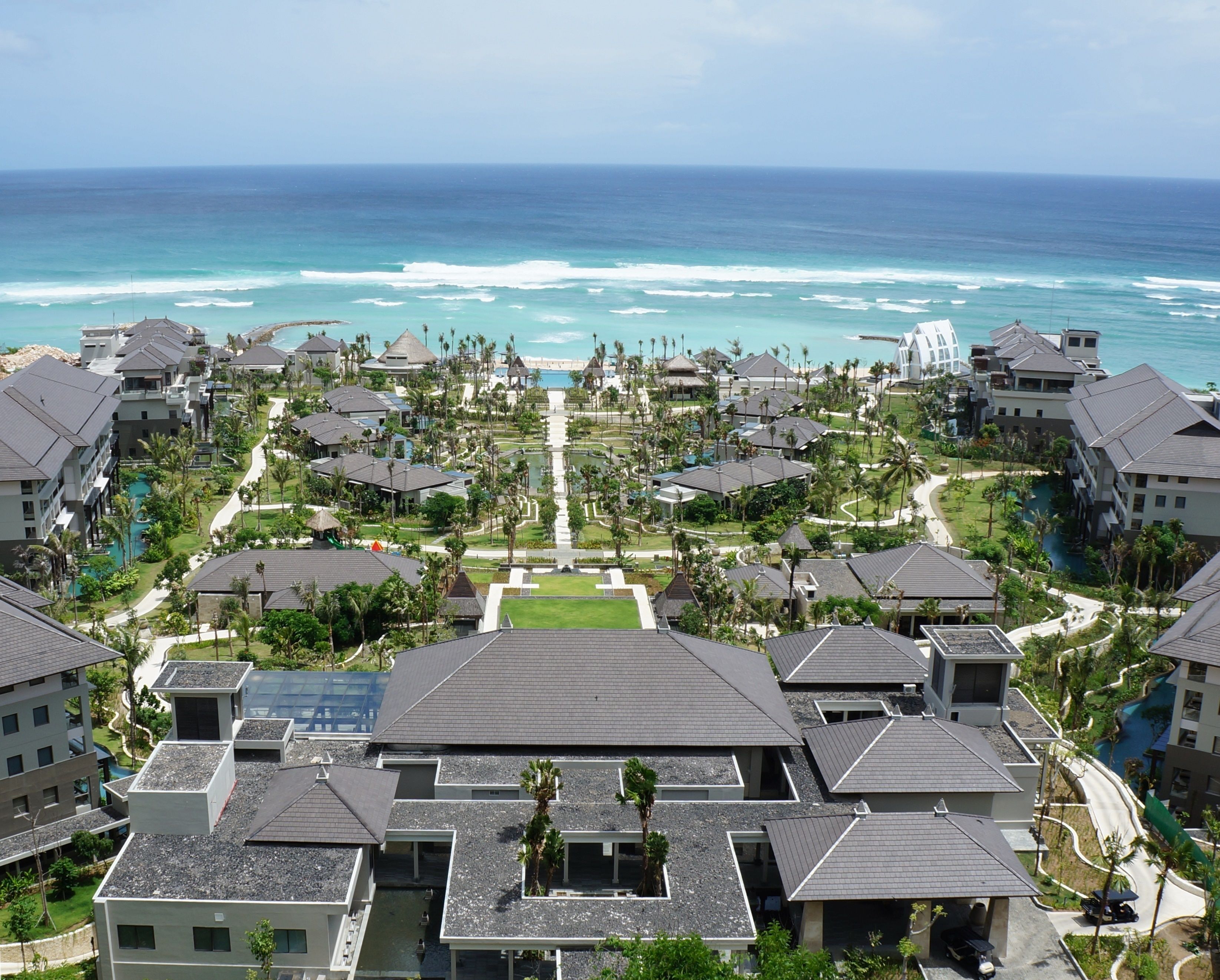 A resort with multiple buildings, a central pathway, and a view of the ocean.