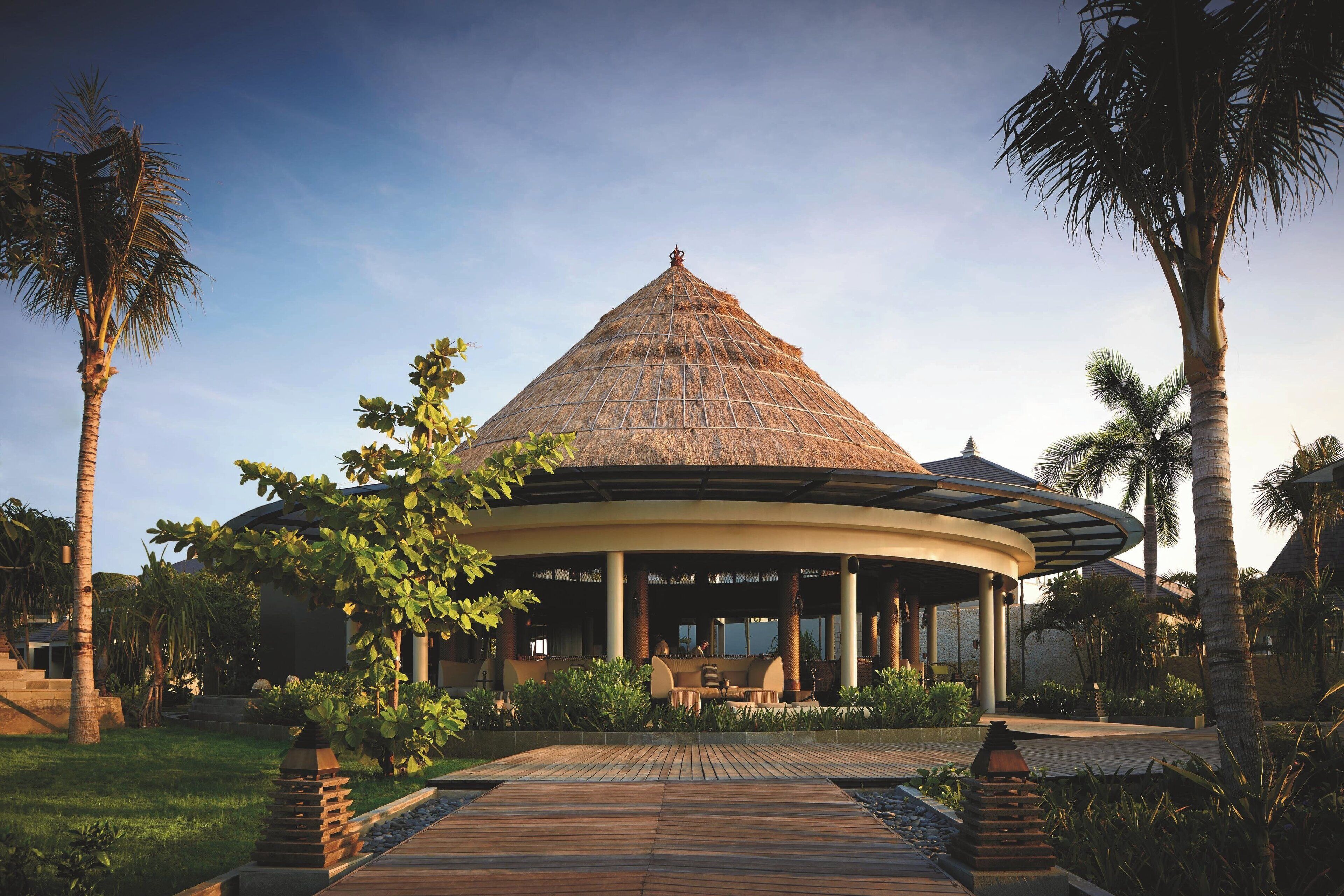 A circular building with a thatched roof, surrounded by palm trees and greenery.