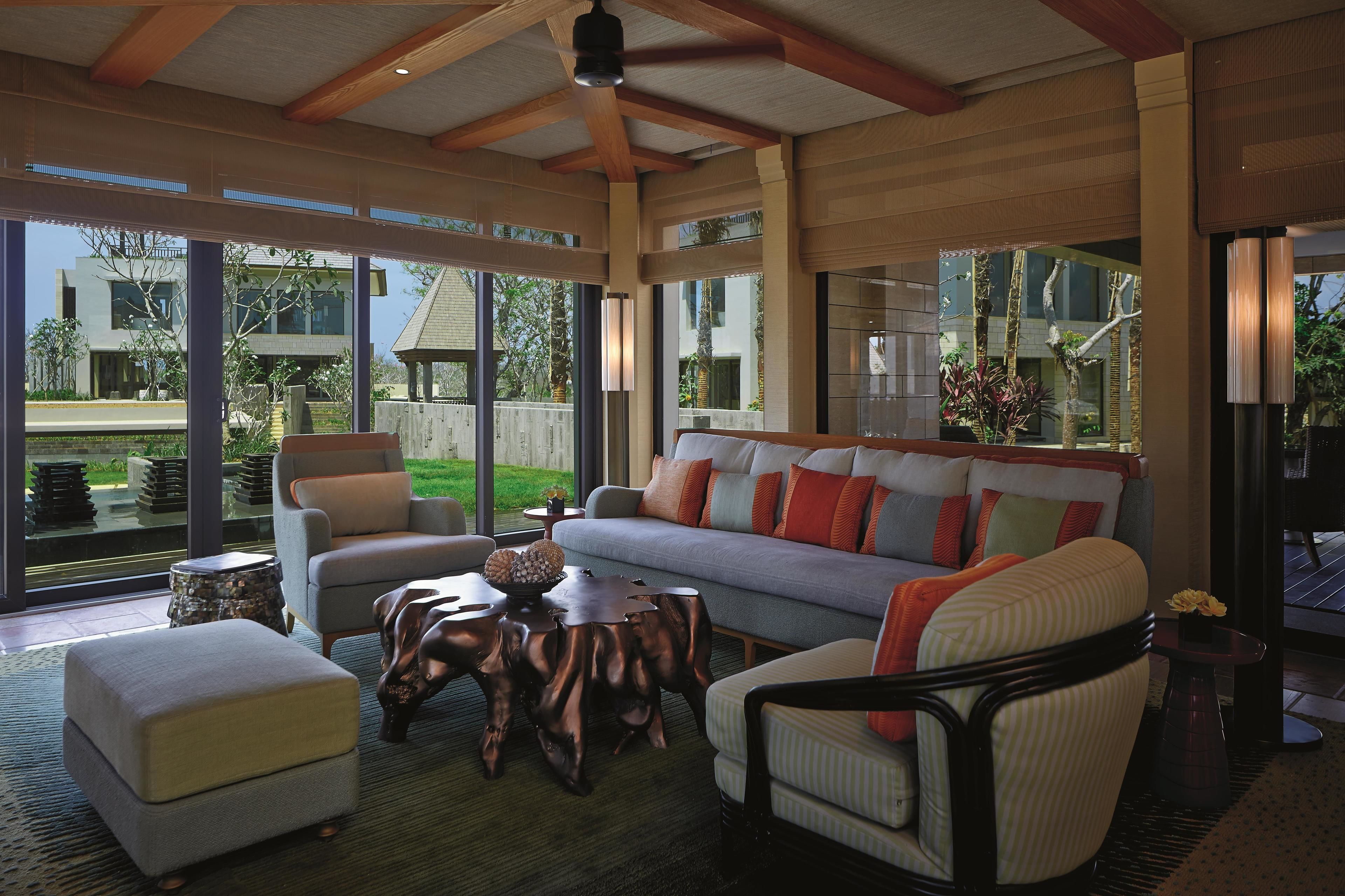 A modern living room with a sofa, armchairs, and a coffee table. Large windows provide a view of the outside.