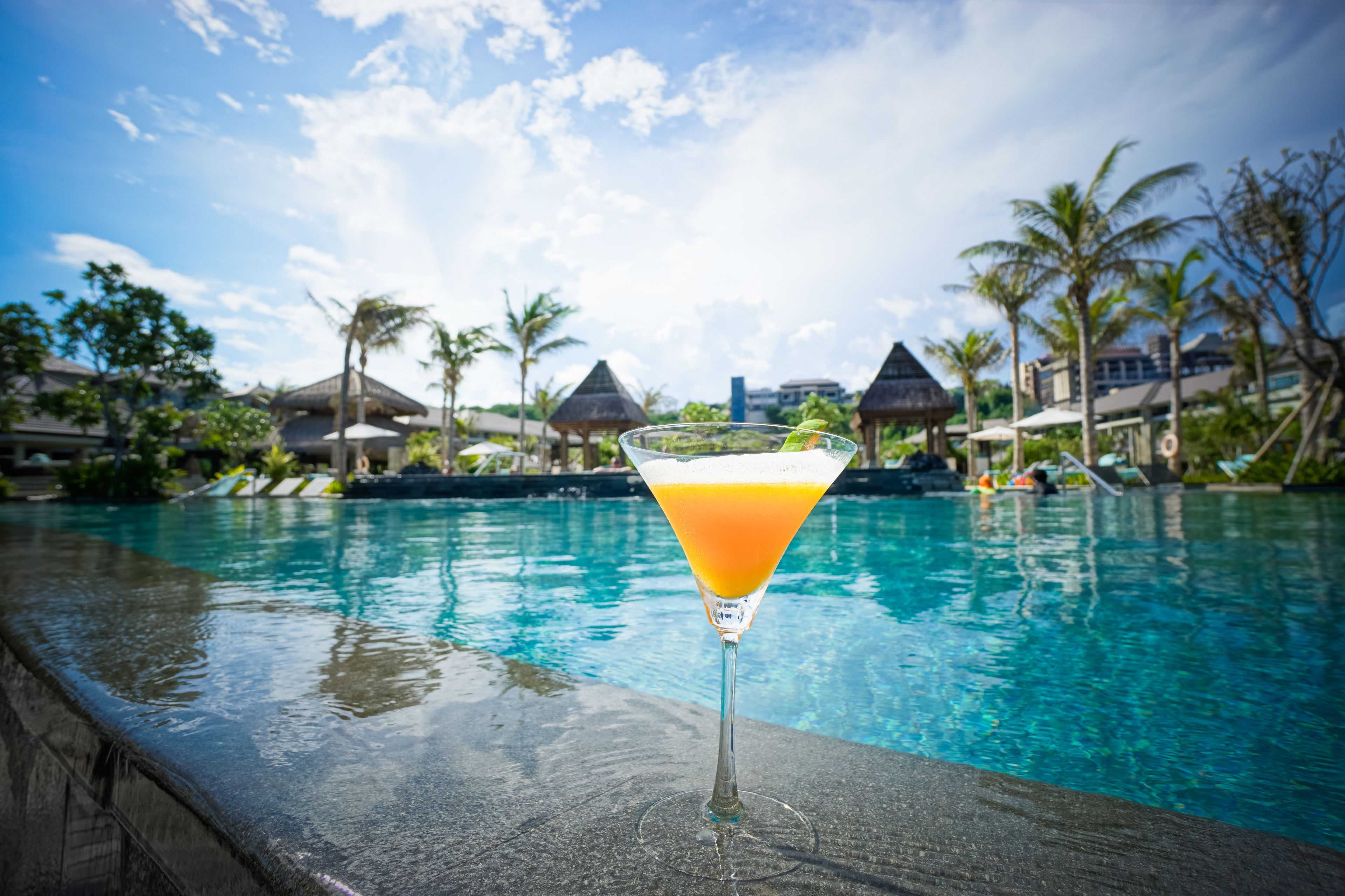A cocktail glass with a tropical drink on a poolside ledge.