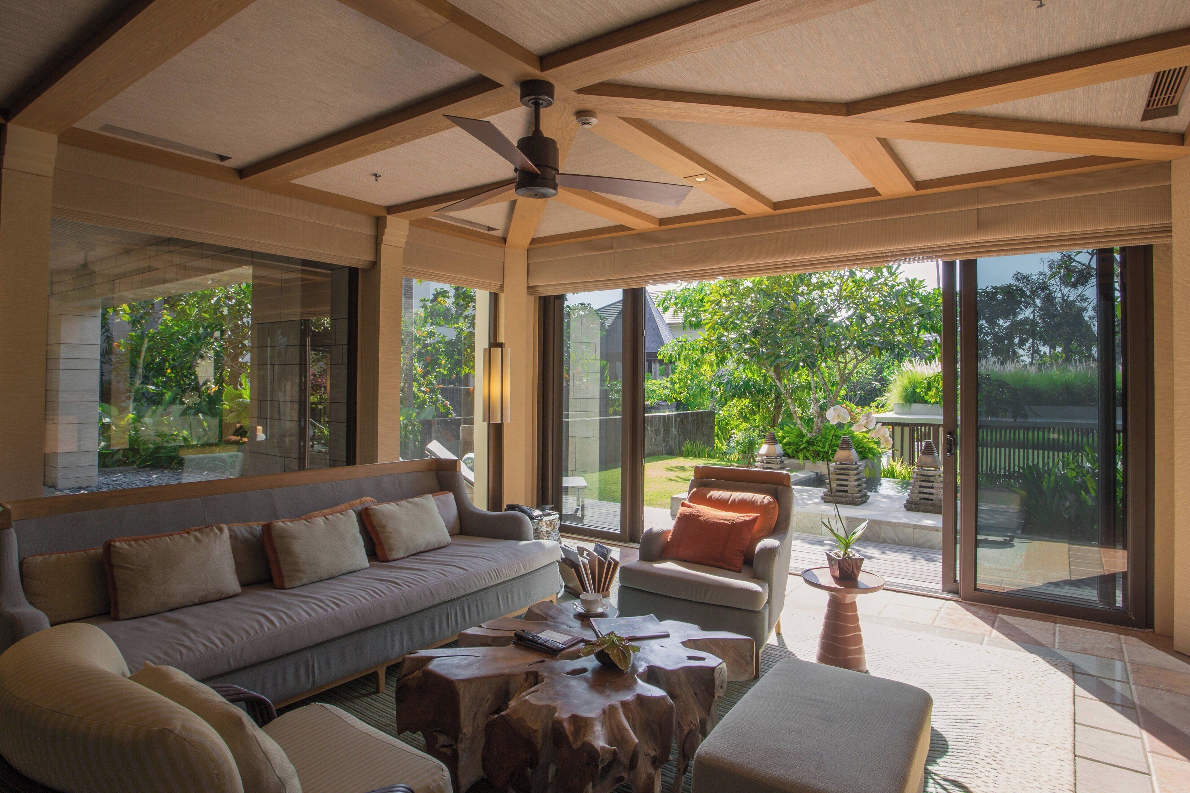 A spacious living room with a large sofa, a coffee table, and a chair. There is a sliding glass door leading to a patio with a view of greenery.