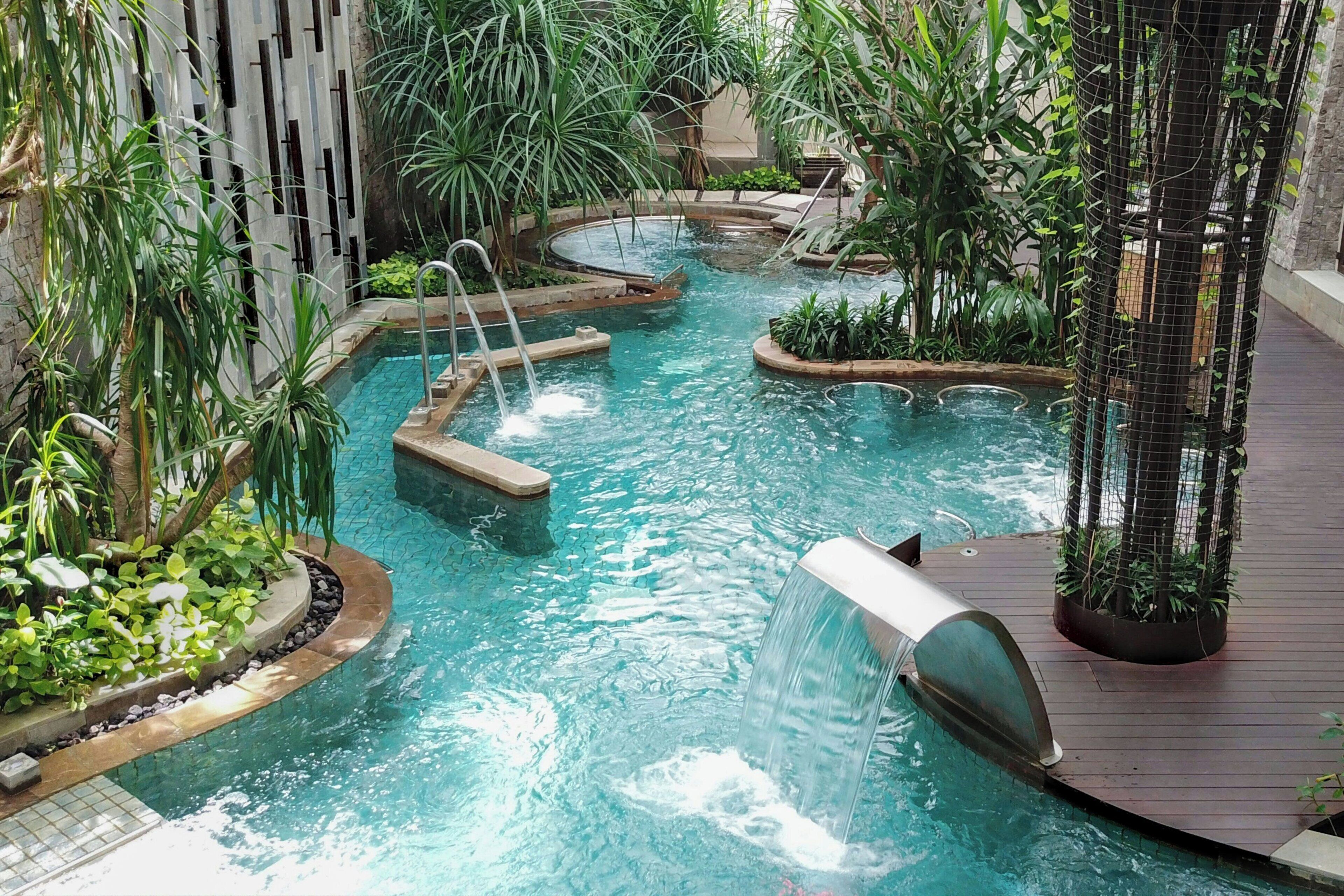 Een binnenzwembad met diverse waterattracties, omgeven door weelderige beplanting en moderne architectuur.