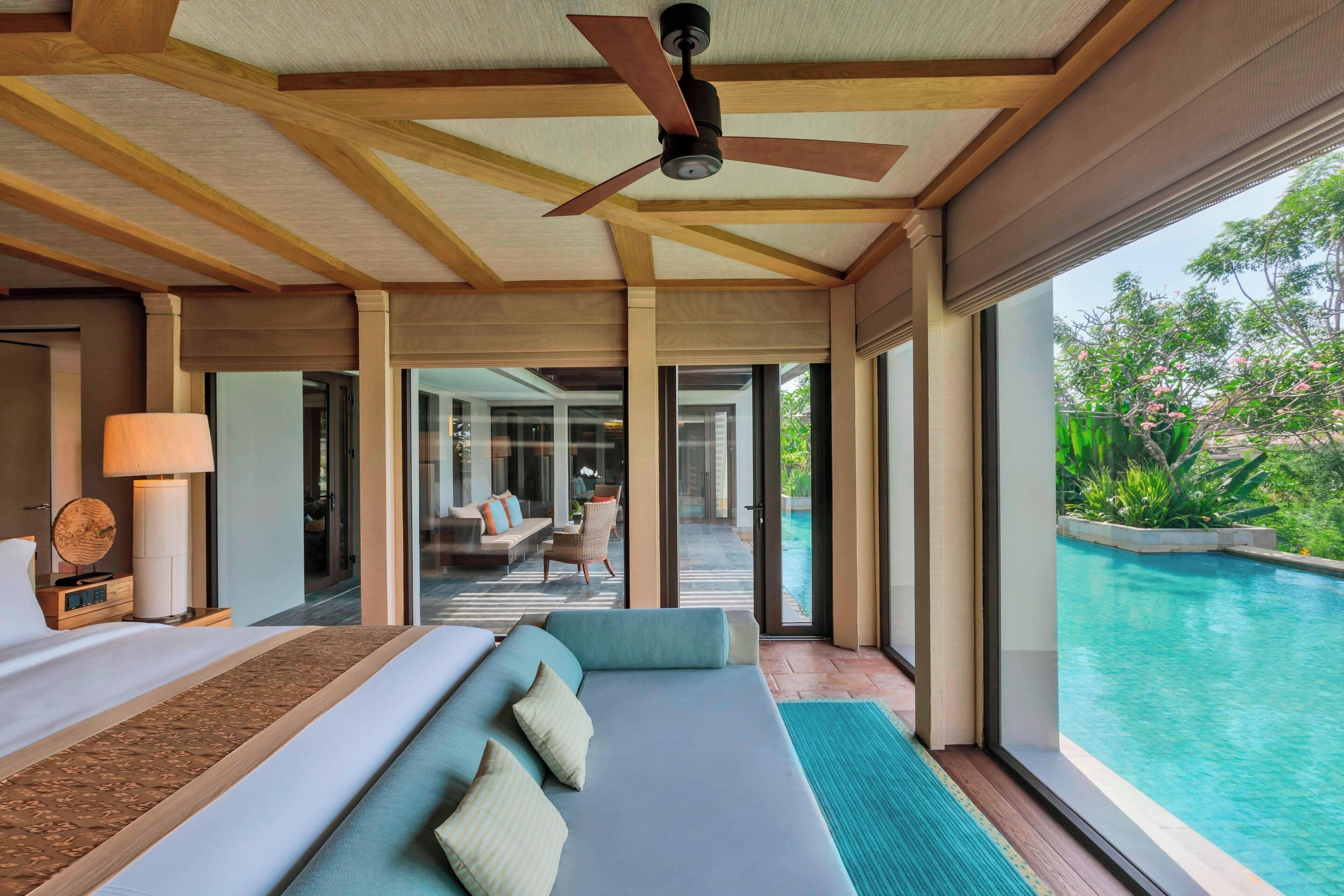 A modern hotel room with a large bed, a ceiling fan, and a view of an outdoor swimming pool.