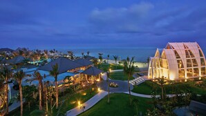 A resort with a pool, palm trees, and a building with a unique architecture. - The Ritz-Carlton, Bali (Nusa Dua)