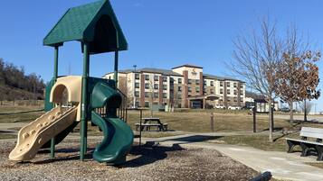 Explore the hotel's outdoor playground with a green slide and a beige slide, surrounded by a gravel area with benches and a picnic table.