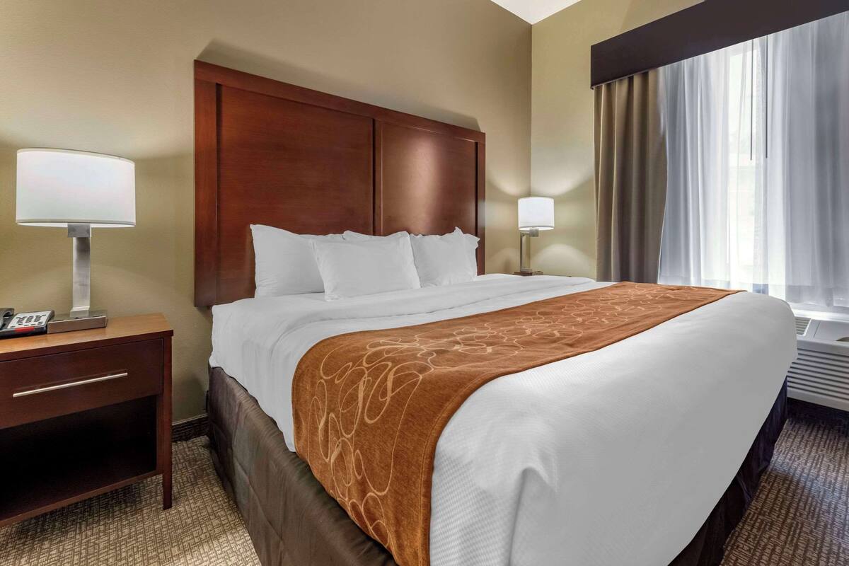 A hotel room with a large bed, wooden headboard, two bedside tables with lamps, and a window with curtains.