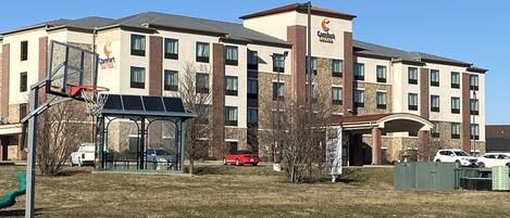 A Comfort Suites hotel with a basketball court and picnic tables in the foreground.