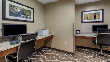 A hotel room with two desks, each with a computer and keyboard, and a chair. There are framed pictures on the walls.
