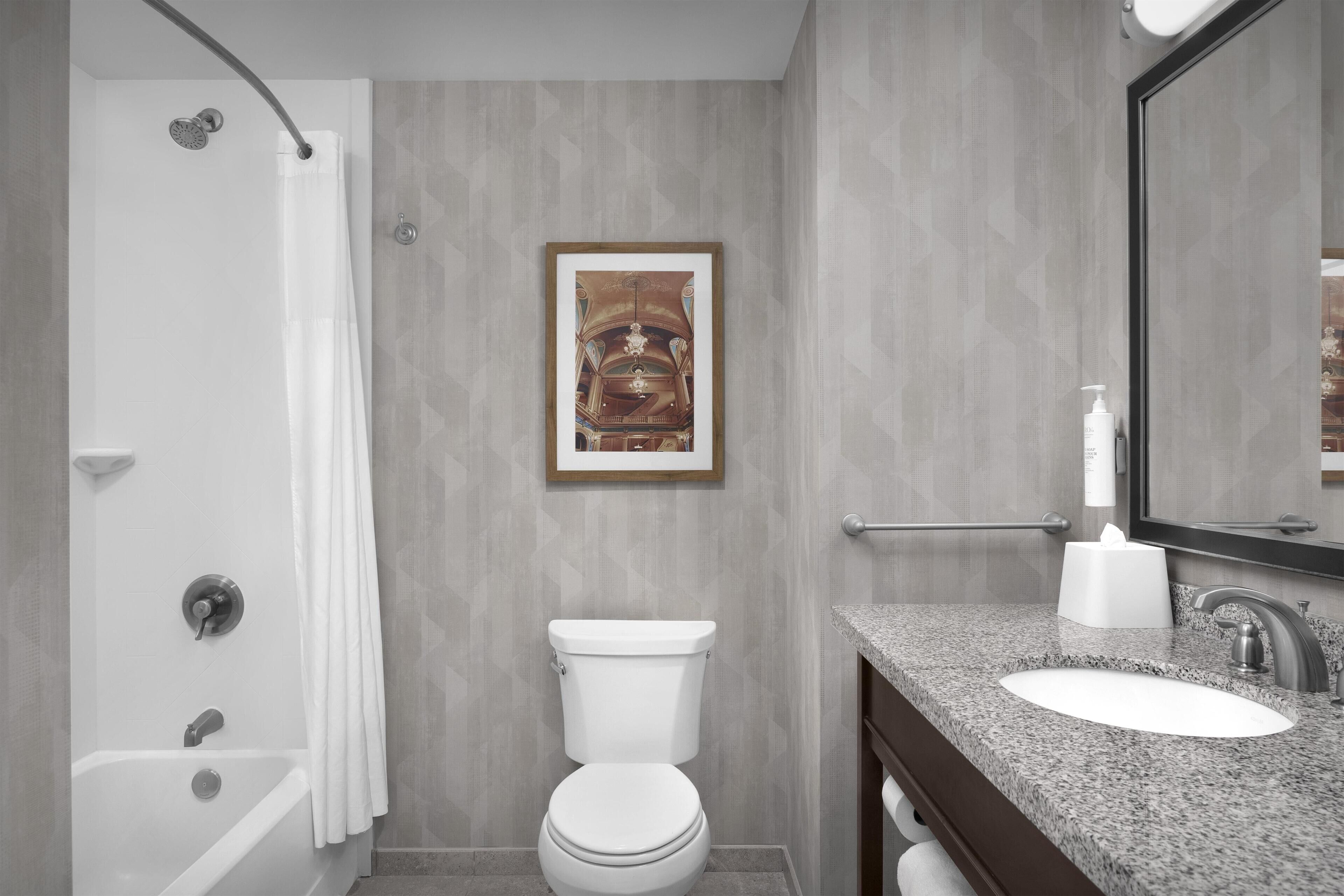 A bathroom with a shower, toilet, sink, and a framed picture on the wall.