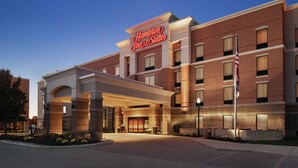 Un hotel Hampton Inn & Suites con fachada de ladrillo, un llamativo letrero de neón y una entrada bien iluminada.