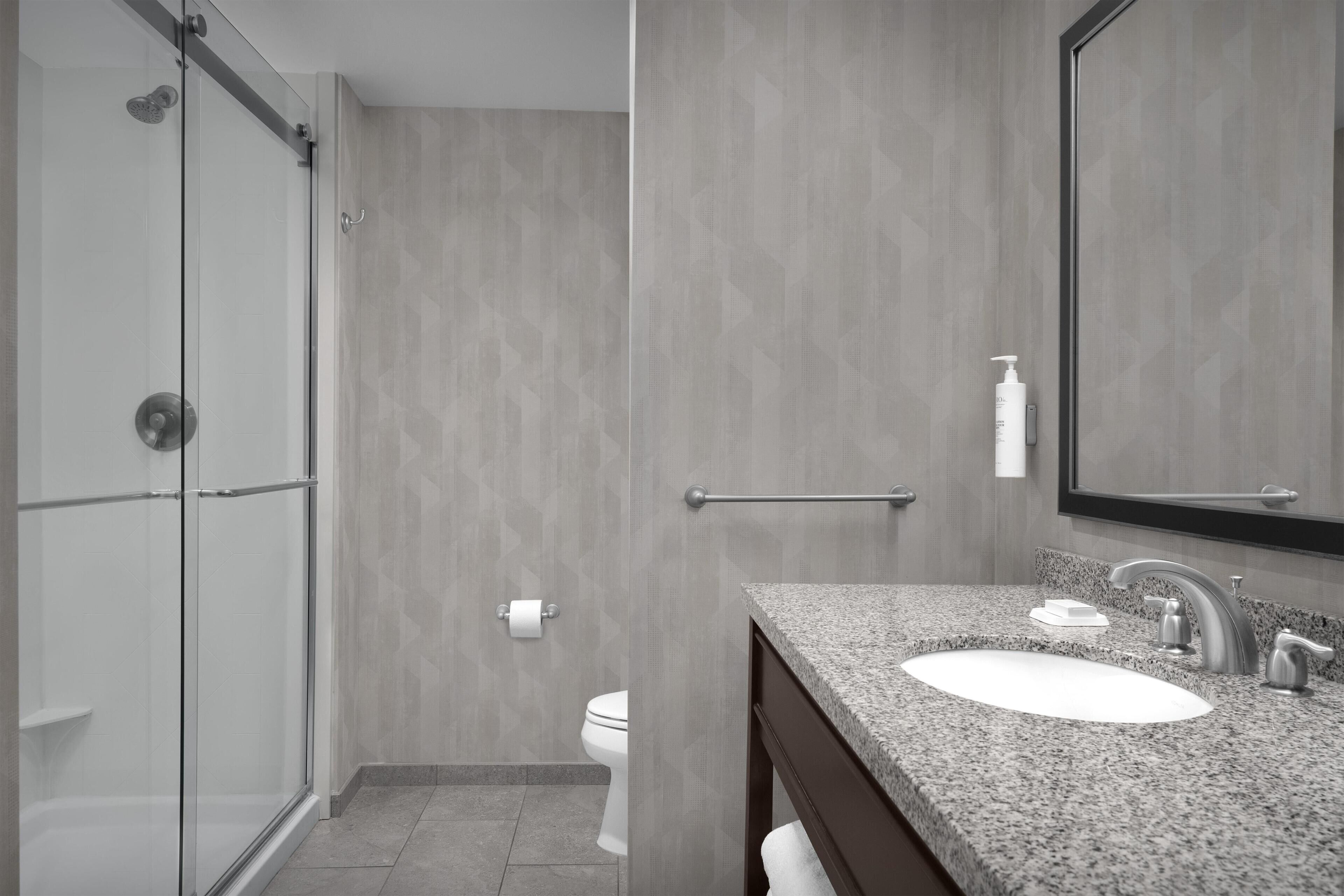 Un baño moderno con cabina de ducha de vidrio, un lavabo con encimera de mármol y un espejo grande.