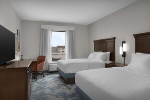 Une chambre d’hôtel avec deux lits, un bureau, une chaise, une télévision et une fenêtre avec des rideaux.