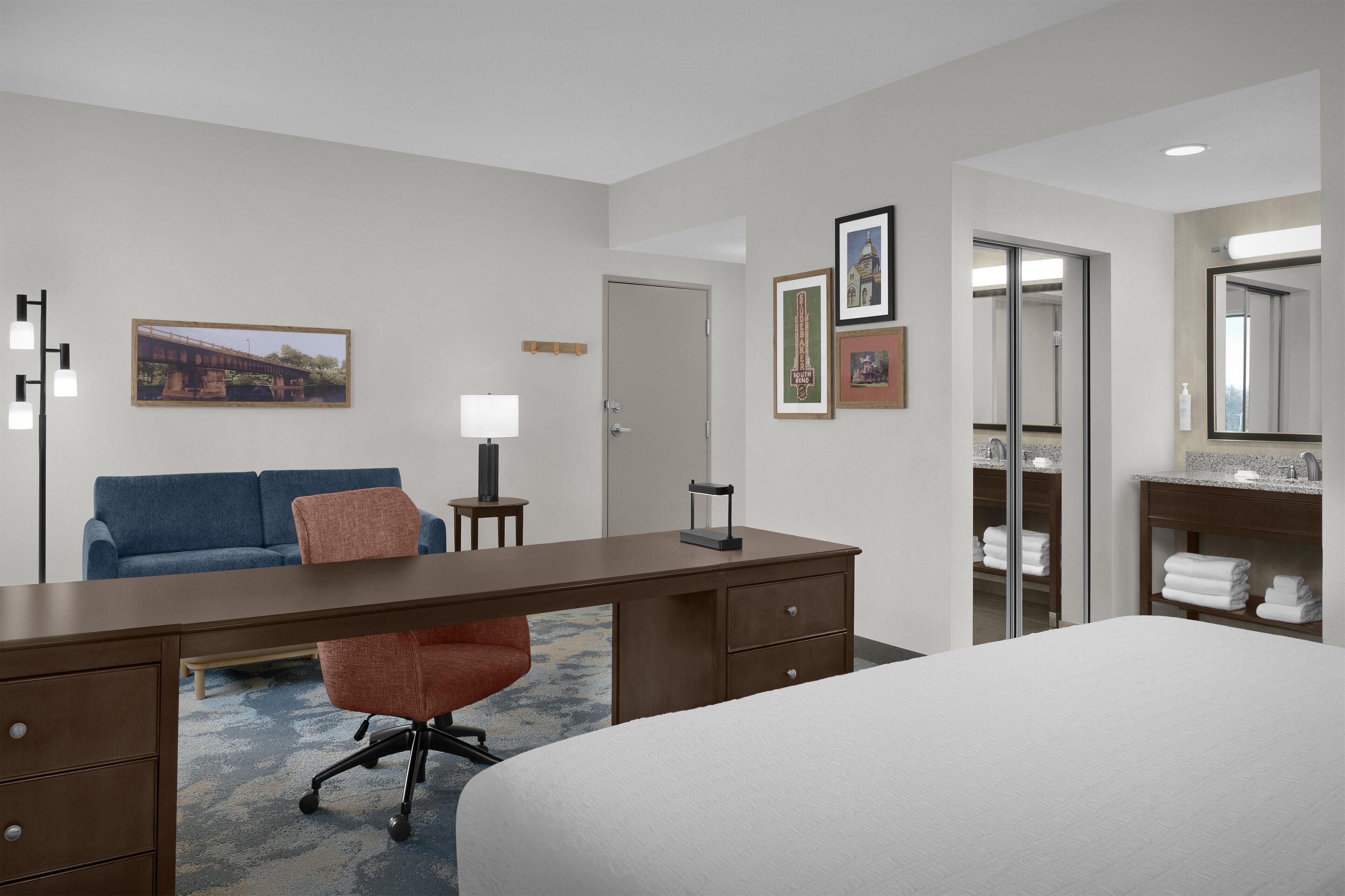 Une chambre d’hôtel comprenant un lit, un bureau, une chaise, un canapé, une lampe, un miroir et une armoire.