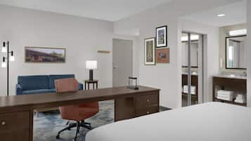 Une chambre d’hôtel comprenant un lit, un bureau, une chaise, un canapé, une lampe, un miroir et une armoire.