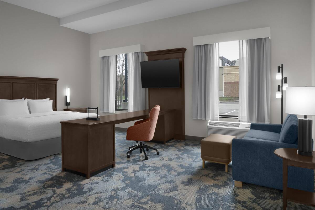 A hotel room with a bed, desk, chair, sofa, and a TV mounted on the wall.