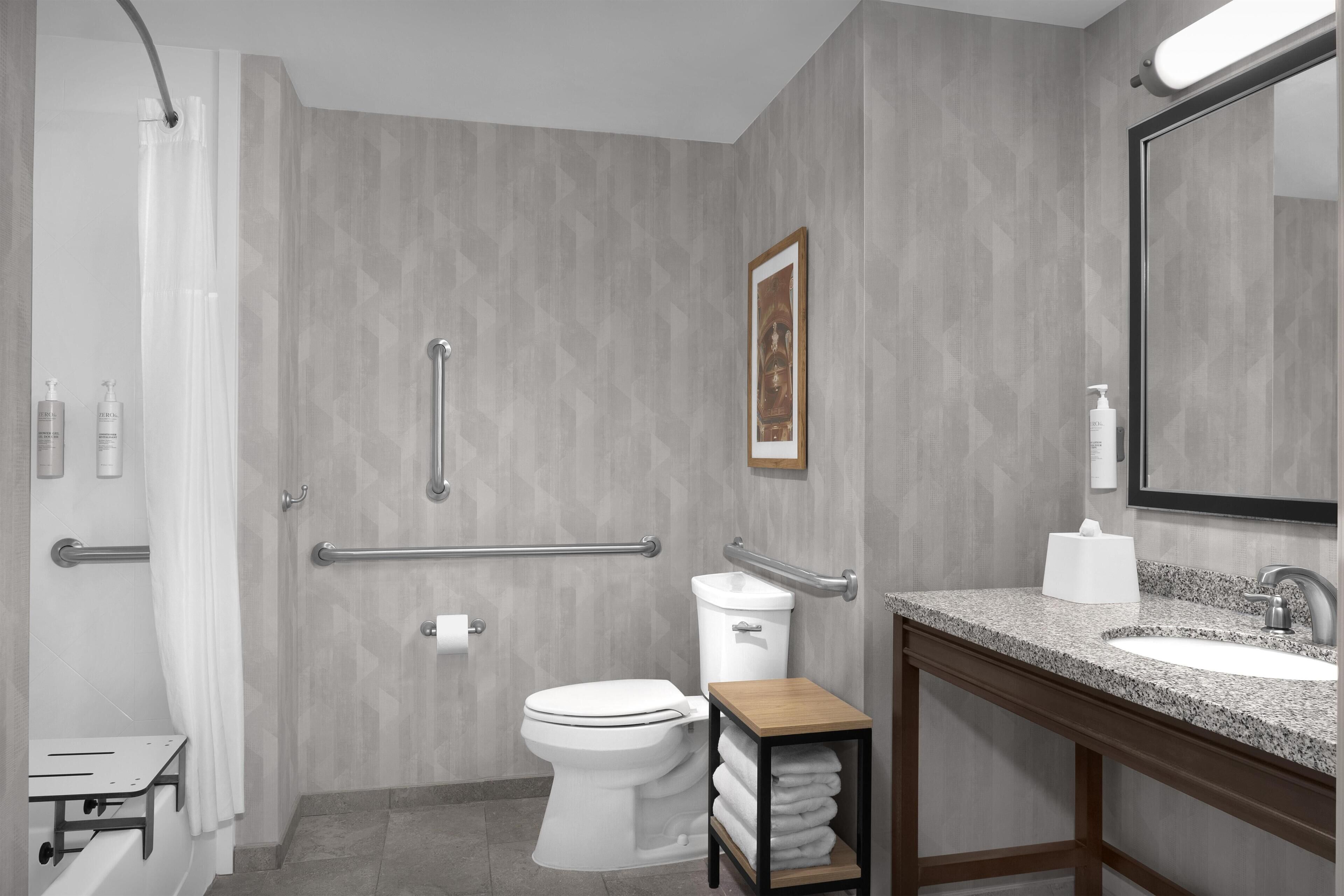 Ein modernes Badezimmer mit Dusche, Toilette und Waschbecken, ausgestattet mit Handläufen und einem Handtuchhalter.