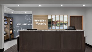 Una recepción con un cartel de 'Welcome to Hampton', vistas a un lago y un letrero de Hilton Honors.