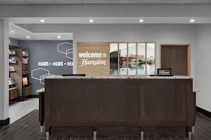 A reception desk with a 'Welcome to Hampton' sign, a view of a lake, and a Hilton Honors sign. - Hampton Inn & Suites Mishawaka/South Bend at Heritage Square (Granger)