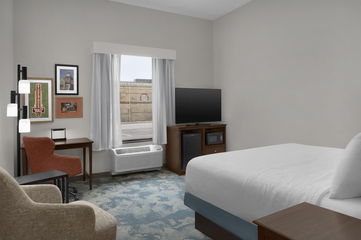 A hotel room with a bed, a desk, a chair, a television, and framed pictures on the wall.