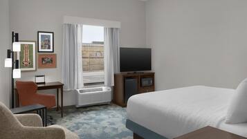 A hotel room with a bed, a desk, a chair, a television, and framed pictures on the wall.
