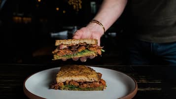 A sandwich on a plate with a person holding it above the plate.
