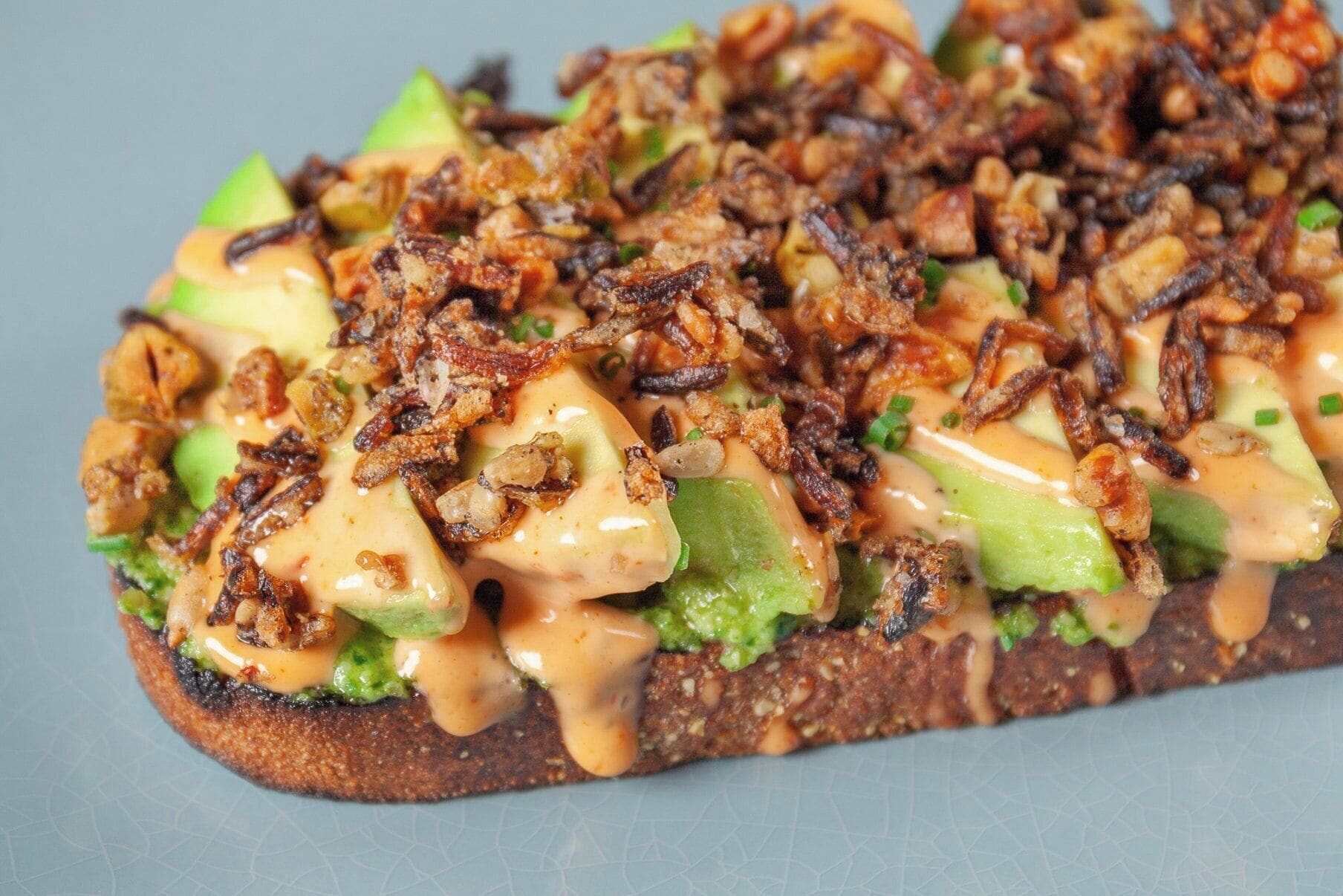 A sandwich with avocado, cheese, and fried onions on a toasted bread.