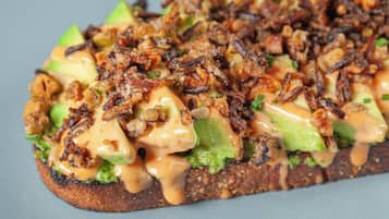 A sandwich with avocado, cheese, and fried onions on a toasted bread.