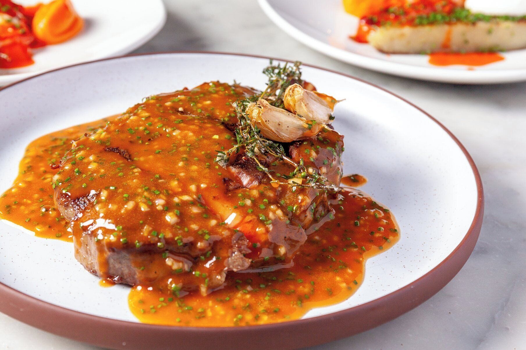 Un plato con un guiso de carne, adornado con hierbas y cebollas, y salsa.