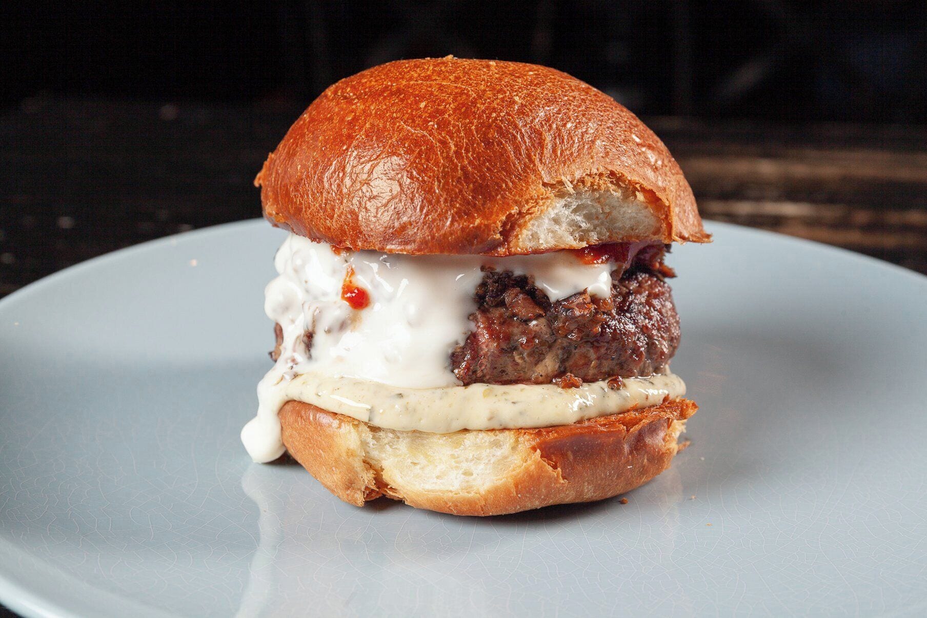 A burger with a bun, meat patty, and sauce on a plate.