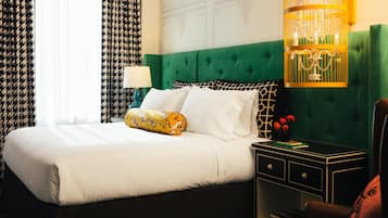 Ein Hotelzimmer mit einem großen Bett, einem mit grünem Stoff gepolsterten Kopfteil, einem Nachttisch mit Lampe und einem dekorativen Vogelkäfig.