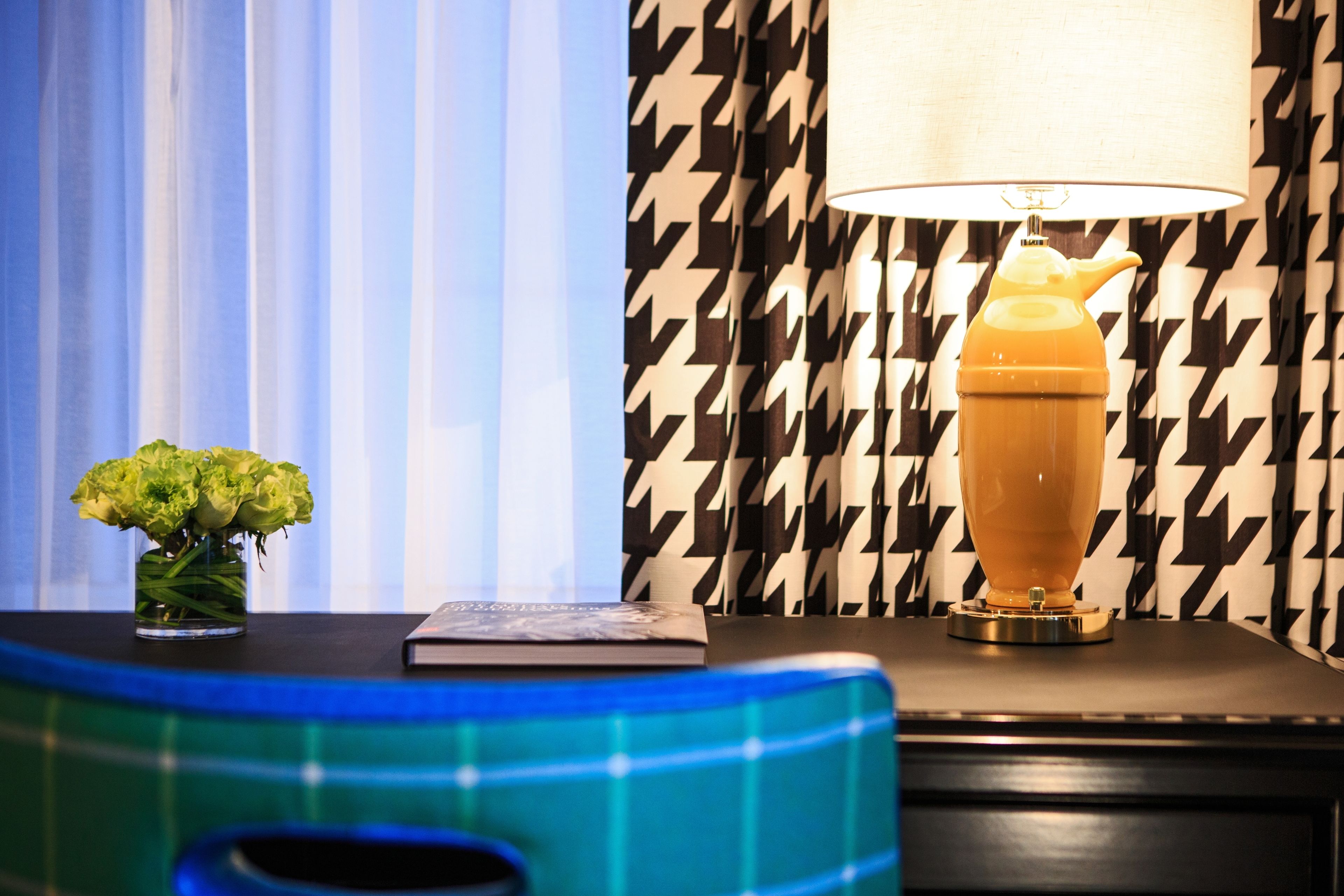 A room with a patterned wall, a lamp, a vase with flowers, and a book on a table.