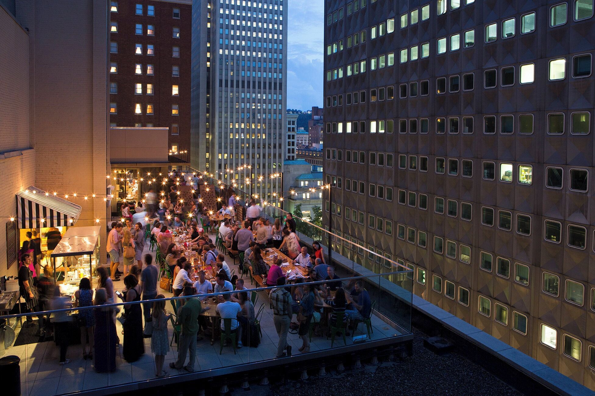 A rooftop dining area with tables and chairs, surrounded by high-rise buildings.