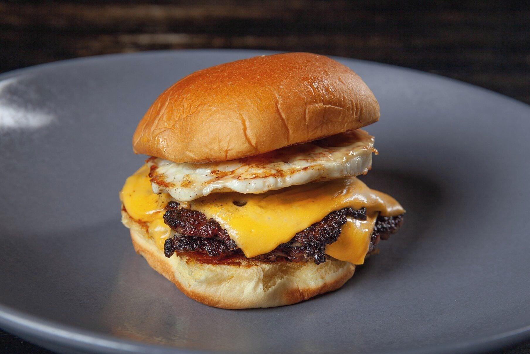 A burger with a toasted bun, egg, cheese, and a beef patty on a plate.