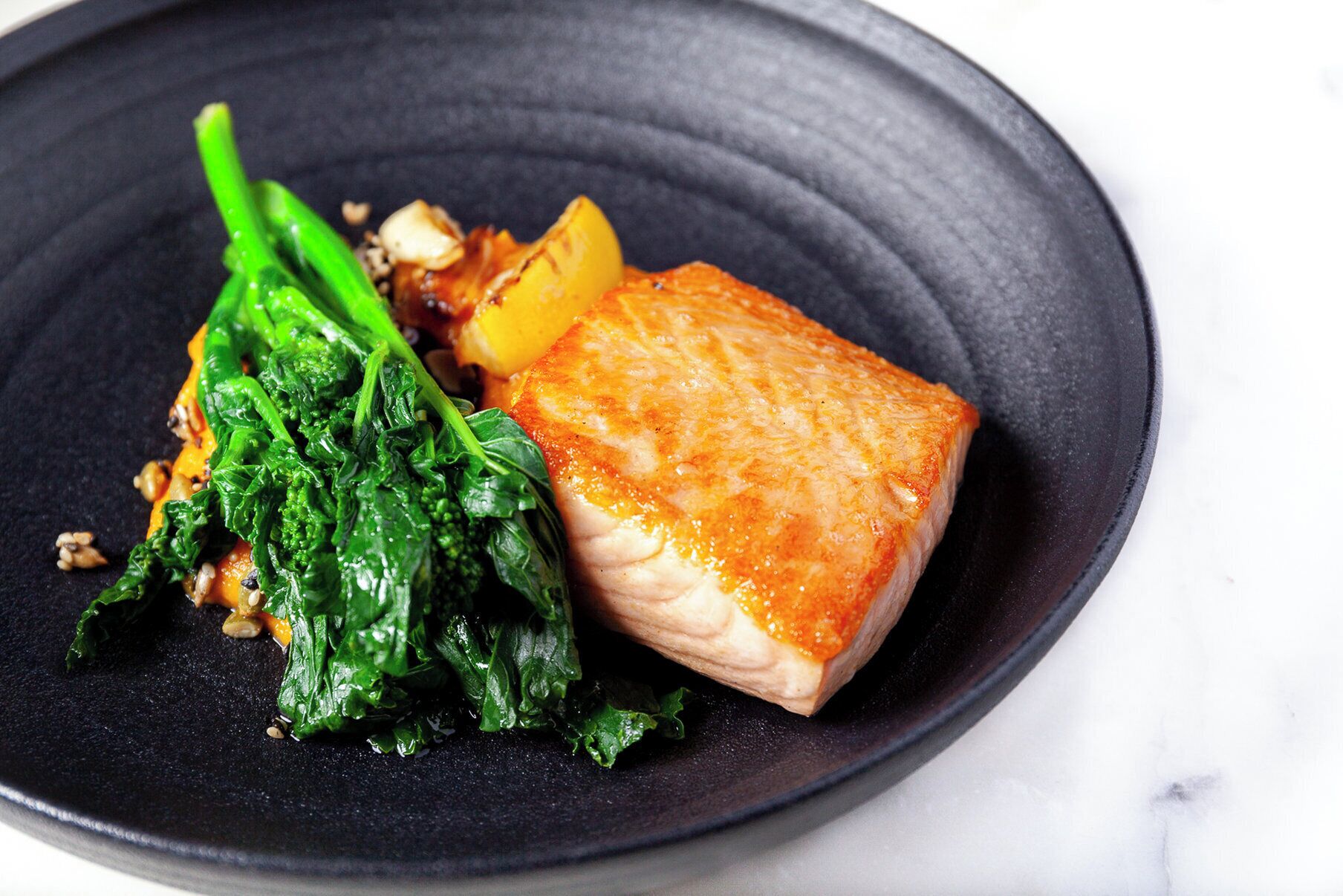 A plate with a piece of salmon, some greens, and a slice of potato.