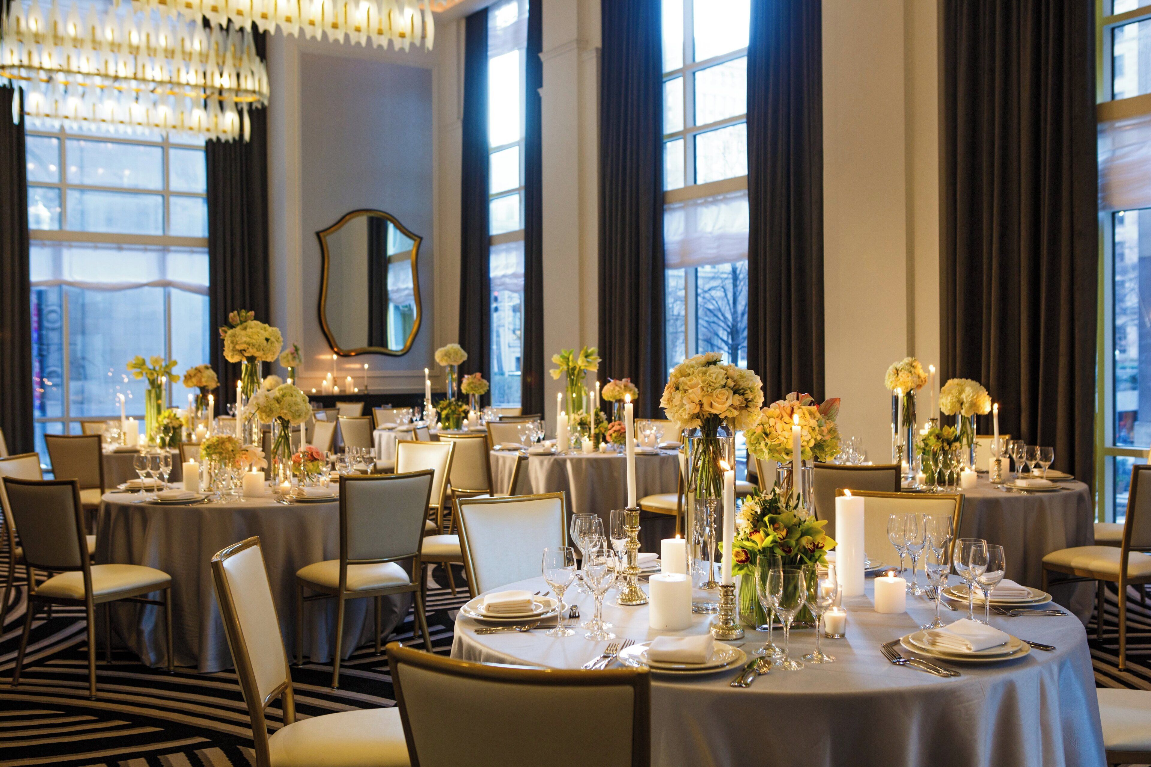 A banquet hall with round tables set for dining, featuring white tablecloths, candles, and floral centerpieces.