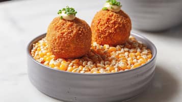 Two breaded balls on a bed of corn kernels in a bowl.